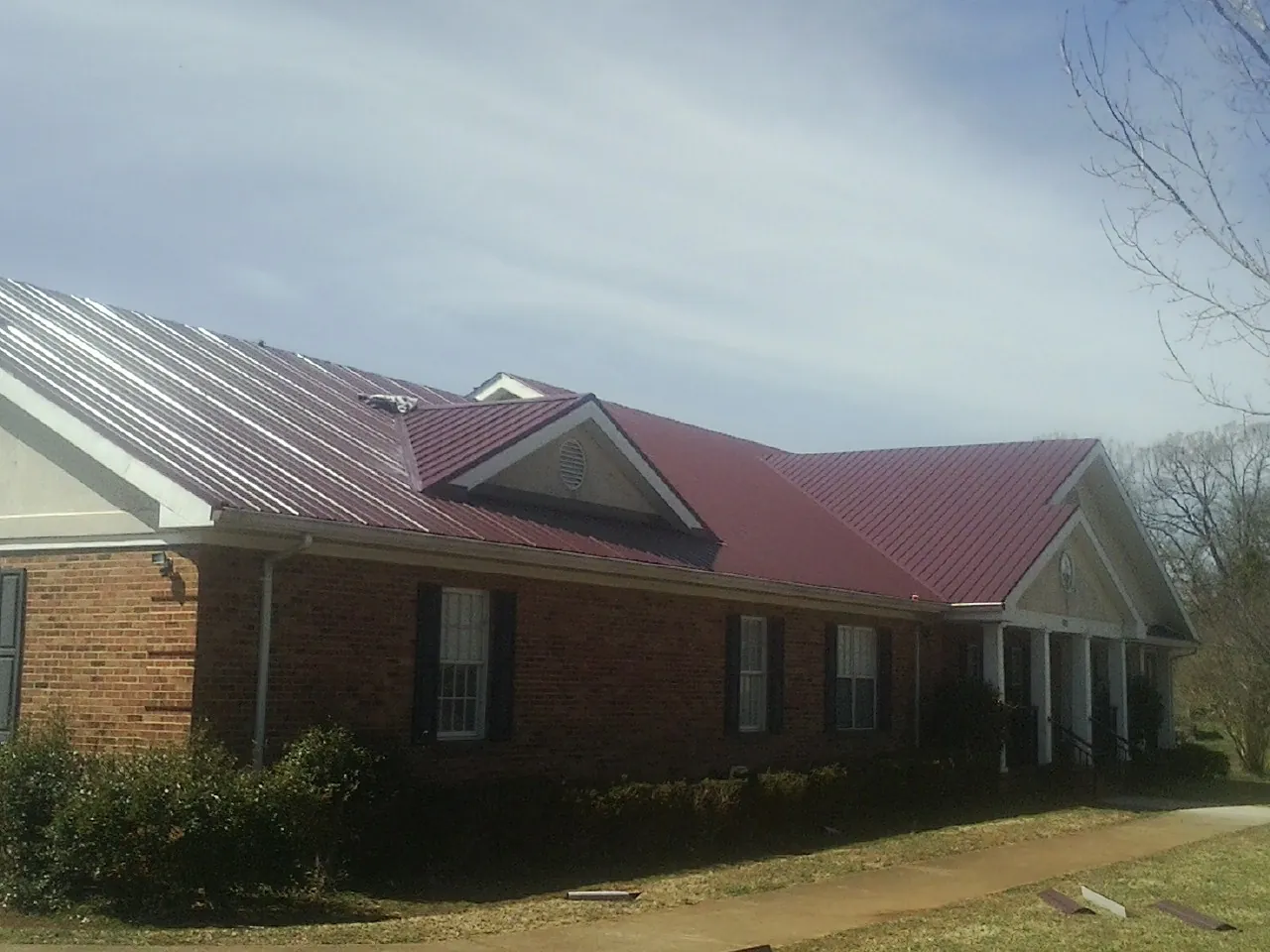 Red metal roof with gabled entries on a long brick building, from a Hail Damage Roof Repair job in Middleburg